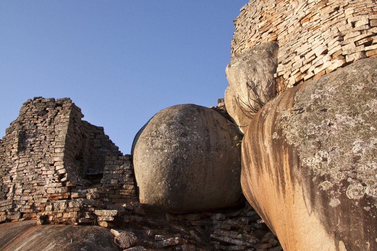 Steinmauer und große Felsen mit Treppe in einer archäologischen Ruine unter blauem Himmel