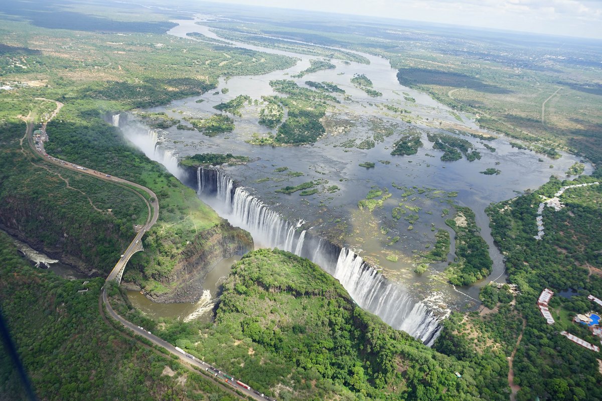 Luftaufnahme der Victoriafälle mit breitem Wasserfall, Flussarmen und umliegender grüner Vegetation