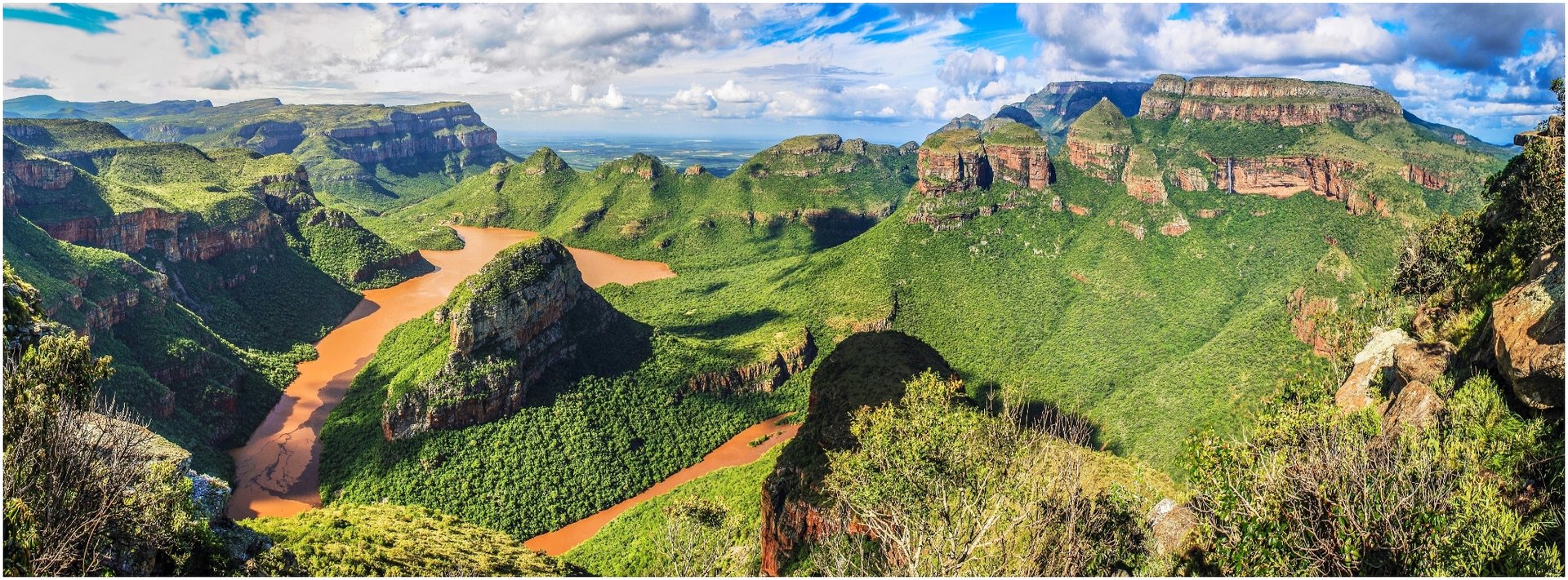 Blick über eine tiefe, grün bewachsene Schlucht, im Hintergrund drei markante, rundliche Felsformationen